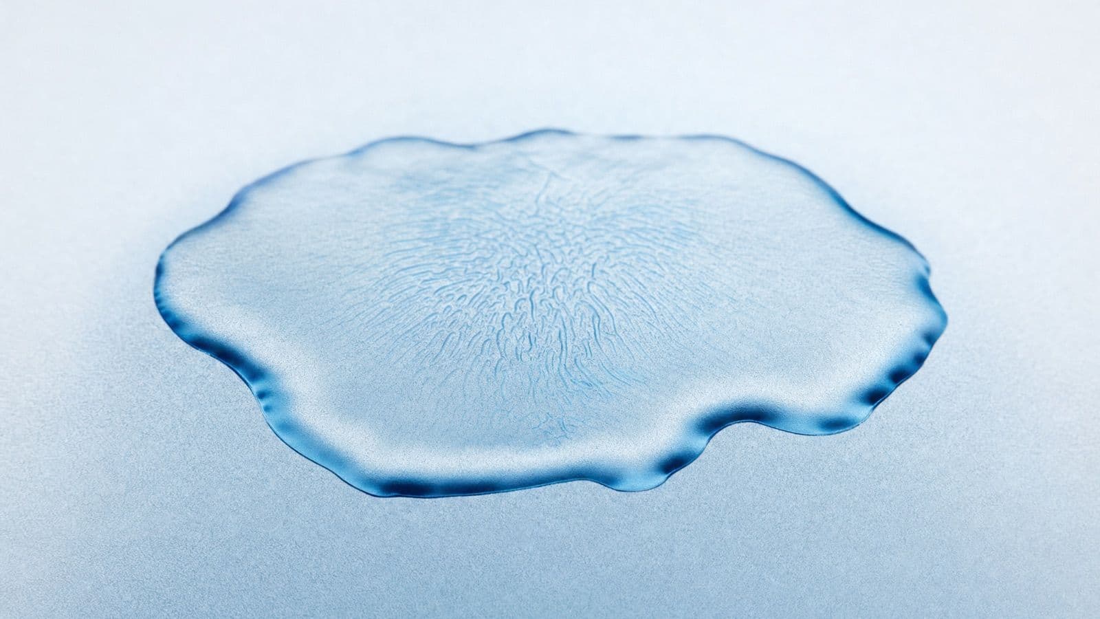 A drop of water spread across frosted glass, its rippled edge catching blue light